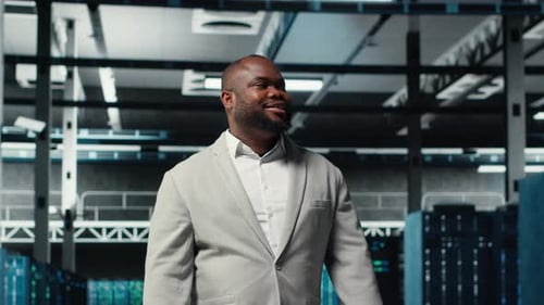 Smiling Engineer Walking in Data Center Checking Hardware for System Stability