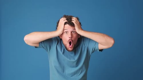 Surprised man looking at the camera with big eyes, says wow, isolated on blue background in studio