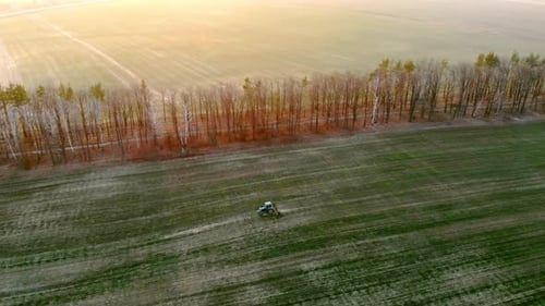 Aerial View Agricultural Tractor Plows a Field at Sunset