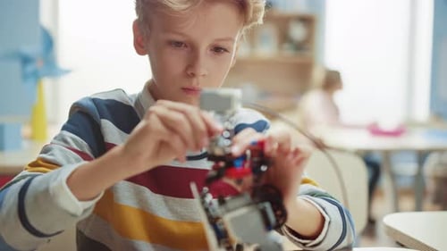 Schuljunge baut/konstruiert kleinen Roboter und programmiert mit Laptop Software für Robotikingenieure