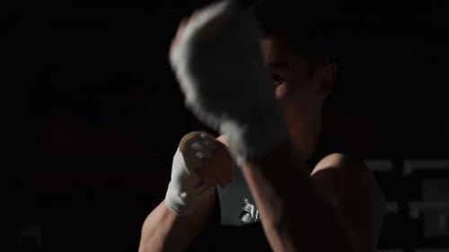 Young Man Training Boxing Punches in Dark Gym
