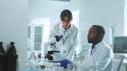 In the Laboratory Two Scientists in Uniform Looking Under a Microscope Talking Discuss Wonder