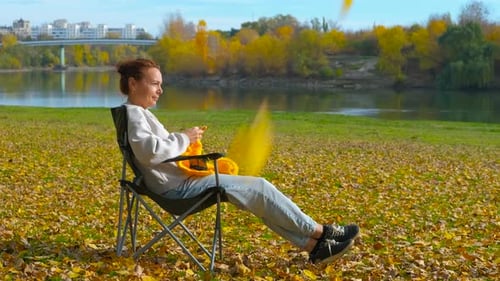 Woman Knitting Relaxing in Autumn Park by River