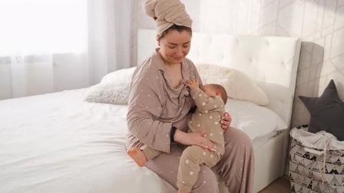 Mother Breastfeeding Baby on White Bed in Bedroom