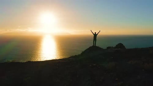 Man Stands on Hilltop Overlooking the Ocean at Sunset