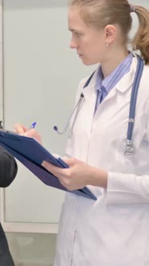 Young Woman Doctor Writes on Clipboard in Hospital Setting