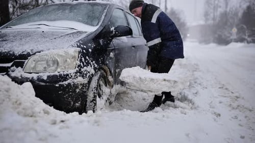 Man Shoveling Snow From Car on a Winter Road Digging Out Vehicle After Heavy Snowfall