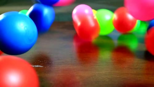 Colorful Plastic Balls Rolling onto Wood Surface