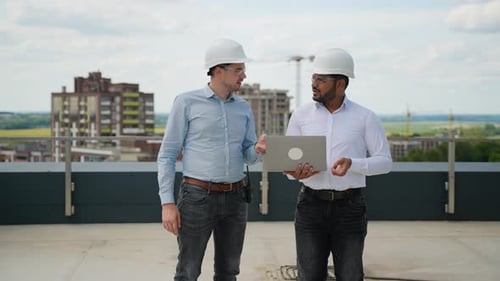 Multiracial Engineers Discussing Project Data on Rooftop Construction Site