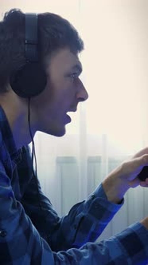 Mann mit Kopfhörern benutzt Controller-Joystick zum Spielen von Videospielen. Vertikales Video