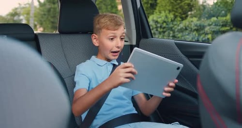 Adolescent assis dans la voiture, ceinture de sécurité attachée pendant le voyage et jouant à des jeux sur tablette PC