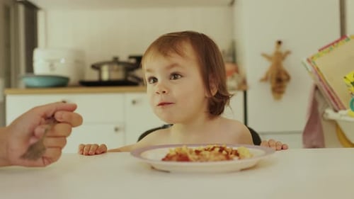 Une mère nourrit un enfant heureux avec des pâtes dans une cuisine lumineuse à table, un enfant joyeux dégustant joyeusement de délicieuses pâtes