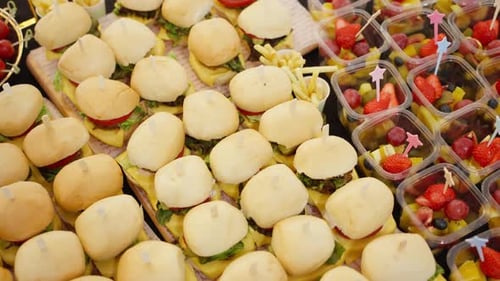 Catering buffet with a variety of appetizers, sandwiches, and fruit cups.