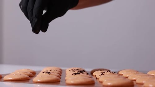 close up of process of making chocolate macarons. chef in black gloves is decorating brown shells
