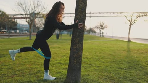 Athletic Woman Exercising Glutes with Resistance Band in Park