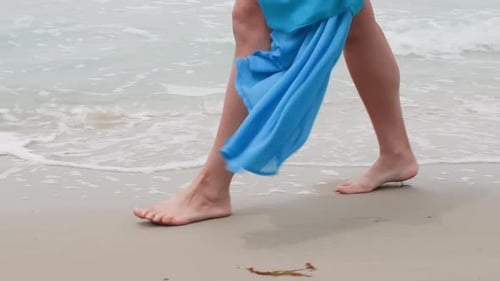 Legs of Woman Tourist Walking on Sandy Ocean Beach Wearing Airy Blue Dress