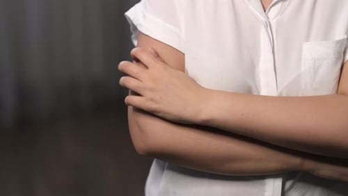 Eine Frau kratzt sich am Arm, ein mögliches Zeichen für psychosomatische Reaktionen, Allergien oder Krankheiten. Es ist ein