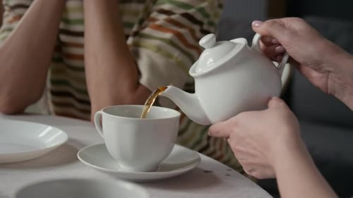 Close-up of Unrecognizable Woman Pouring Tea from White Teapot Into Teacup