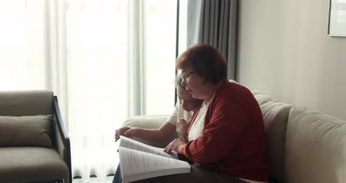 Grandmother and Child Reading Book Together on Sofa