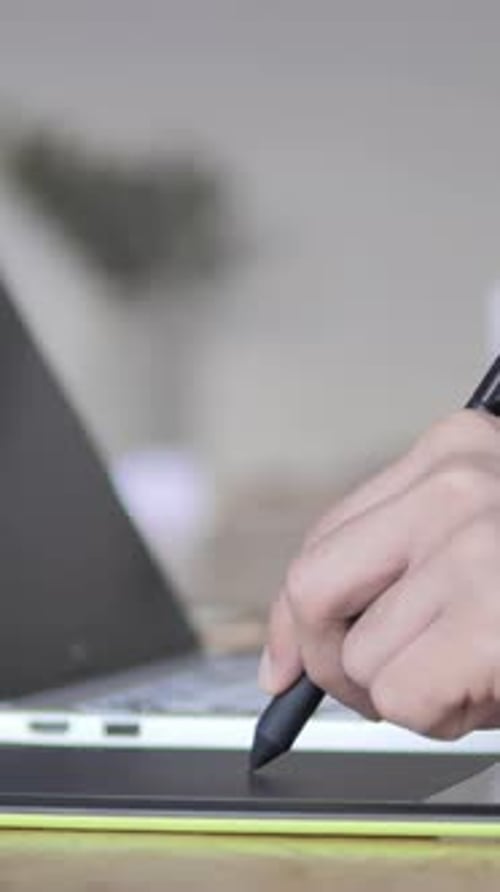 Hand Using Stylus on Tablet with Laptop Nearby