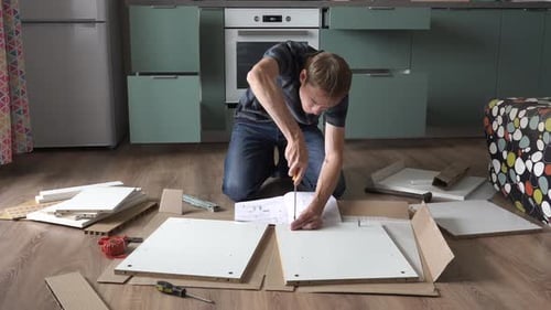 Man Assembling Furniture in Kitchen With Screwdriver