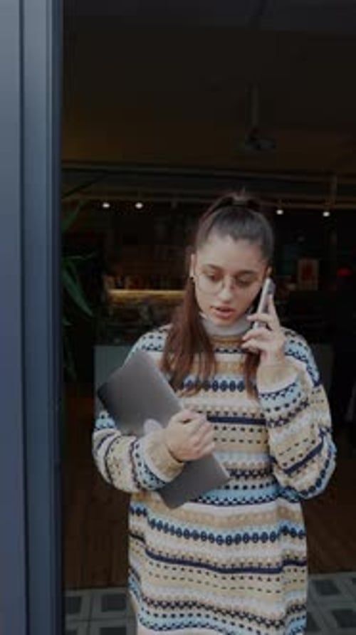 Jovem mulher está falando ao telefone enquanto sai do café