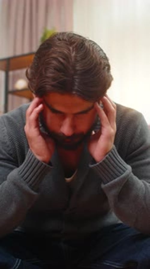 Worried Man Massaging Temples Sitting in Living Room
