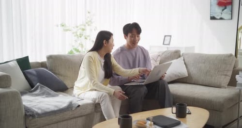 Young Adults Looking at Laptop on Sofa at Home