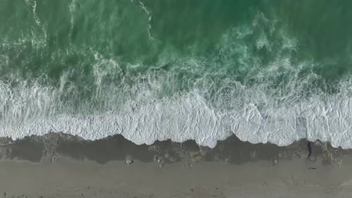 Aerial Video Stormy Waves Roll in Bringing Beautiful Foam Textures to the Tranquil Beach