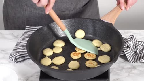 Person cooking mini pancakes in skillet