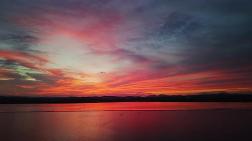 Puesta de sol vívida sobre un tranquilo lago salado que refleja tonos rojos, naranjas y morados bajo un cielo dramático