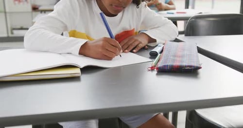 Video of african american schoolboy sitting at desk writing in school class