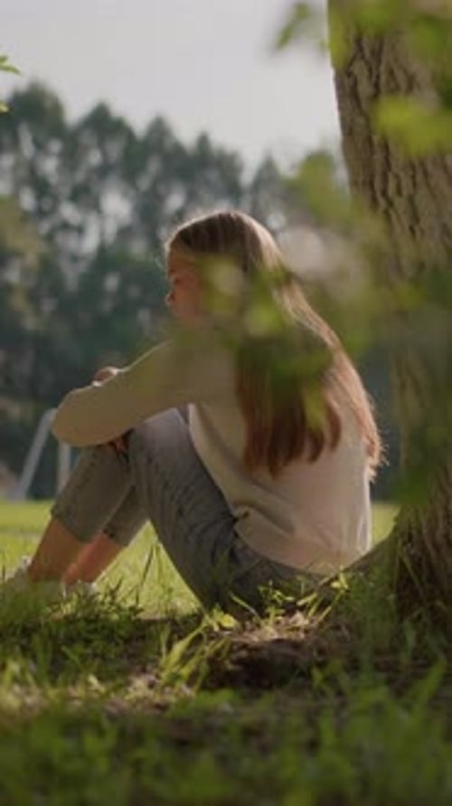 Thoughtful Woman Sitting on Grass in Sunlit Park Surrounded By Greenery