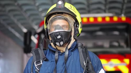 Portrait of Male Firefighter in Protective Helmet and Uniform Standing Near a Big Red Car at Station