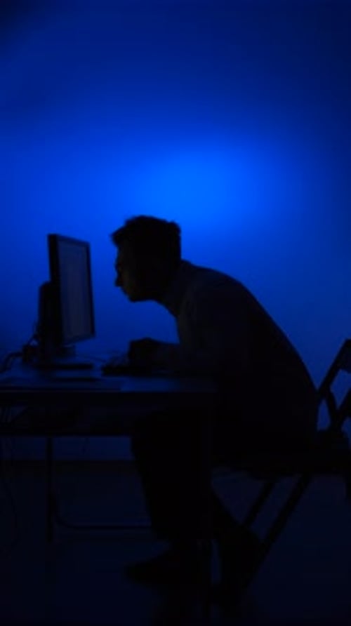Vidéo verticale : un homme travaille tard devant un ordinateur avec une lumière bleue