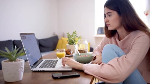 Woman Using Laptop While Eating Breakfast at Home