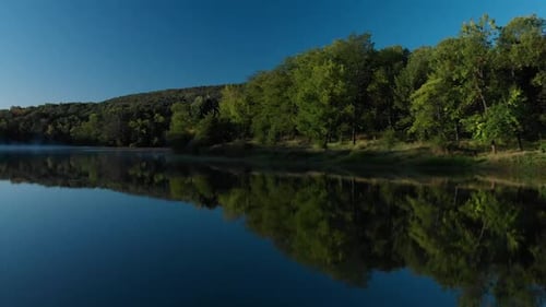 Early morning low drone shot over glossy lake and some fog