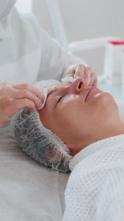 Cosmetologist Doctor Wipes Woman Face and Eyes Cleaning Procedure with Cotton Wipes in Beauty Clinic