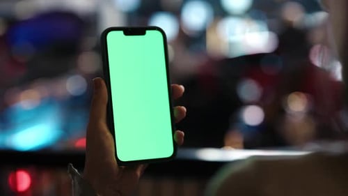 Frau hält Handy in der Hand und schaut Chroma Key an, der auf der Nachtstraße steht