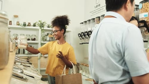 A young woman is shopping in refill store with reusable bag, zero-waste grocery.