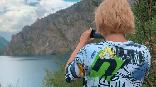 Tourist woman blonde shoots on phone scenic views clear lake and mountains, make video