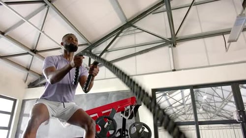 Using battle ropes, african american man working out in gym for fitness and strength training