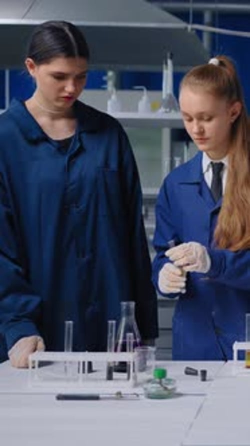 Young Scientists in Protective Lab Coats Conducting Chemical Experiment with Glassware and Colorful