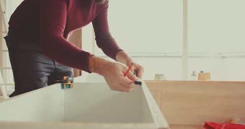 skilled man measures with a tape and marks with a pencil on the furniture piece he's building. Preci