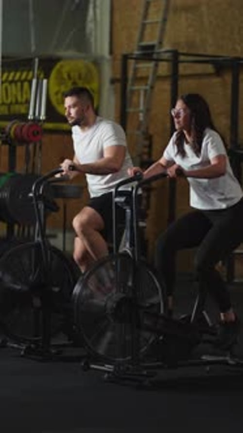 Pareja atlética que hace ejercicio intensamente en bicicletas de aire estacionarias durante una sesión de cardio