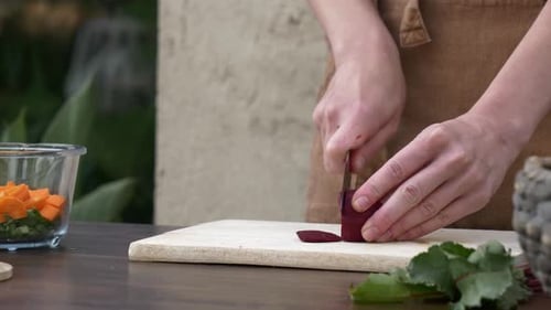Woman in brown clothes cooking vegetable salad, cut beet with knife on board, Wroclaw, Poland