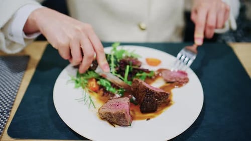 Woman cutting a medium rare steak served with vegetables and sauce on a restaurant plate