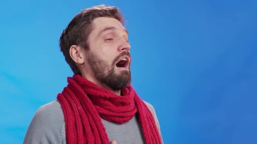Man with Scarf Sneezing Against Blue Background
