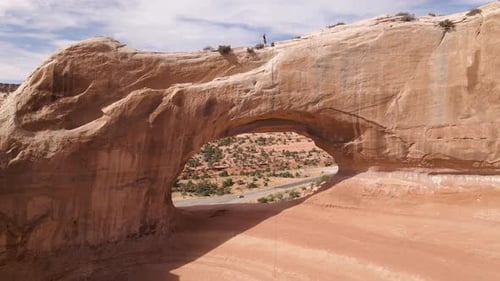 Aerial backward of man walking over Wilson Arch rock formation, Utah. USA