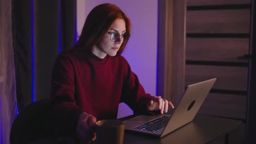 A Determined and Focused Redhaired Programmer Woman is Working Late Into the Night on Her Laptop in